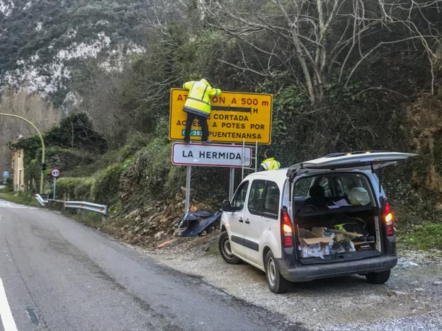 Dos operarios de Carreteras quitan la lona al cartel que informa de los cortes en la carretera del Desfiladero de La Hermida