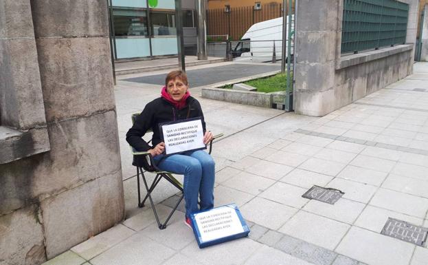 Silvia Martínez, con su nuevo cartel de protesta, sentada en una silla que llevó de su casa en la acera ante el Gobierno de Cantabria.