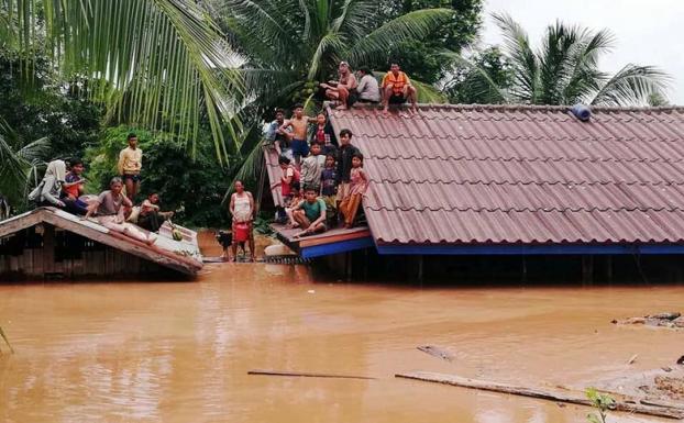 Un grupo de personas aguarda en lo alto de un tejado en una zona inundada.