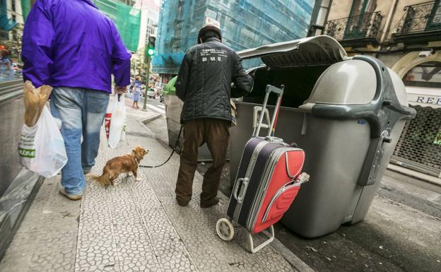 Un hombre busca en un cubo de basura. 