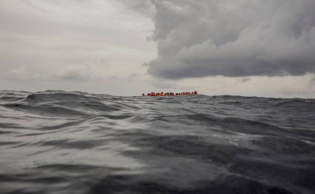 la fotografía en la que se ve a lo lejos los migrantes, con sus chalecos salvavidas, en la inmensidad de un mar y un cielo teñidos de gris.