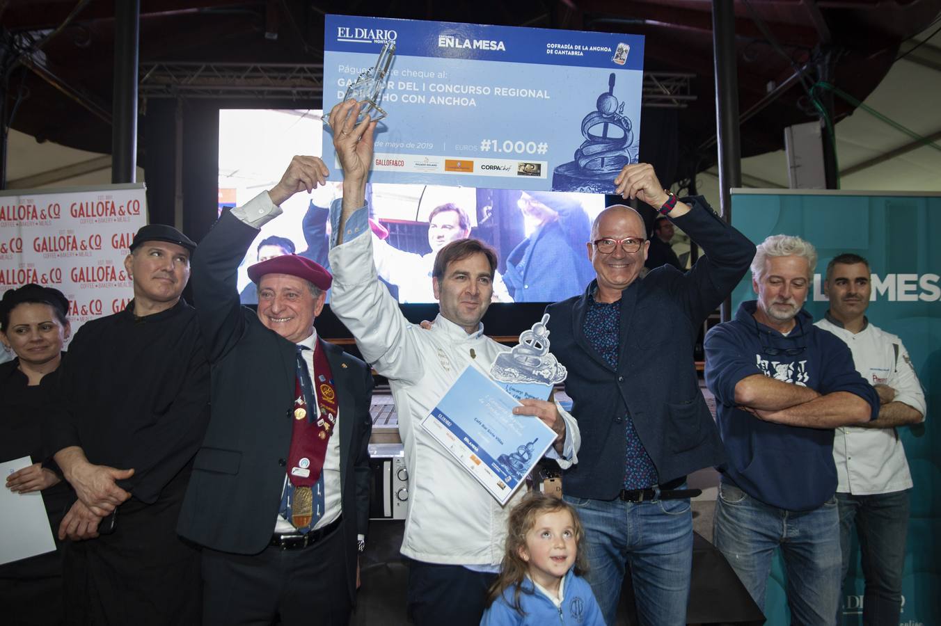 El presidente de la Cofradía de la Anchoa de Cantabria, Tino Sampedro, y Pedro López, de El Diario, sostienen el talón que recibe Sebastián Larralde, ganador del concurso. Abajo, su hija Valentina.