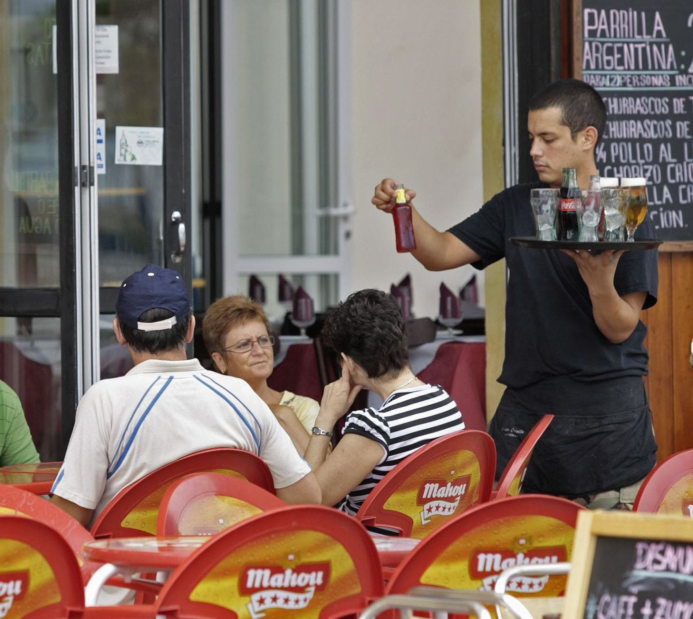 Un camarero sirve unas bebidas a unos clientes en una terraza de verano.