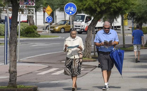 Imagen reciente de turistas paseando por El Sardinero con ropa de verano y acompañados de un paraguas. 