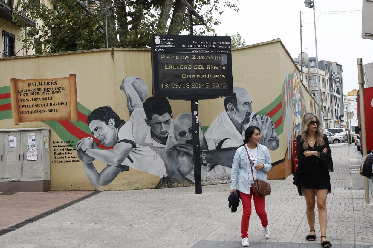 Dos mujeres caminan junto a uno de los paneles de la calidad del aire, ubicado en la zona de El Zapatón.