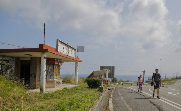 Dos peregrinos del Camino del Norte pasan junto a un viejo puesto de socorro de la Cruz Roja en la N-634 antes de coronar Saltacaballo.