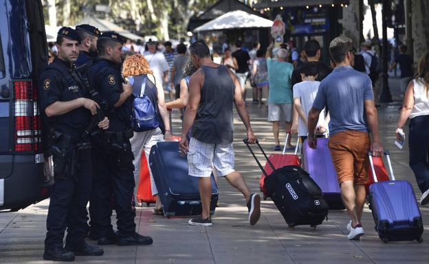 Agentes de policía vigilan La Rambla mientras un grupo de turistas pasa con maletas. 