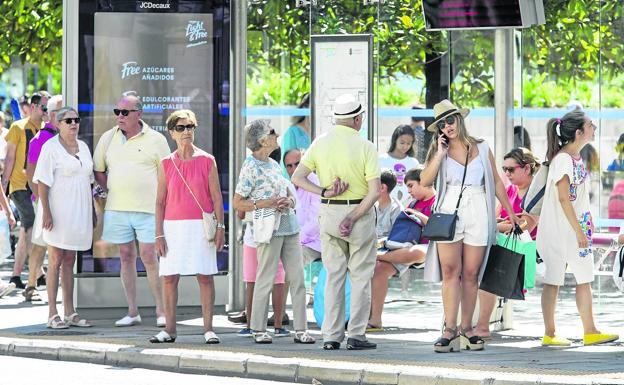 Al bus. Un grupo de personas espera en la parada de Correos. Los buses pasan constantemente llenos de gente camino a la playa.