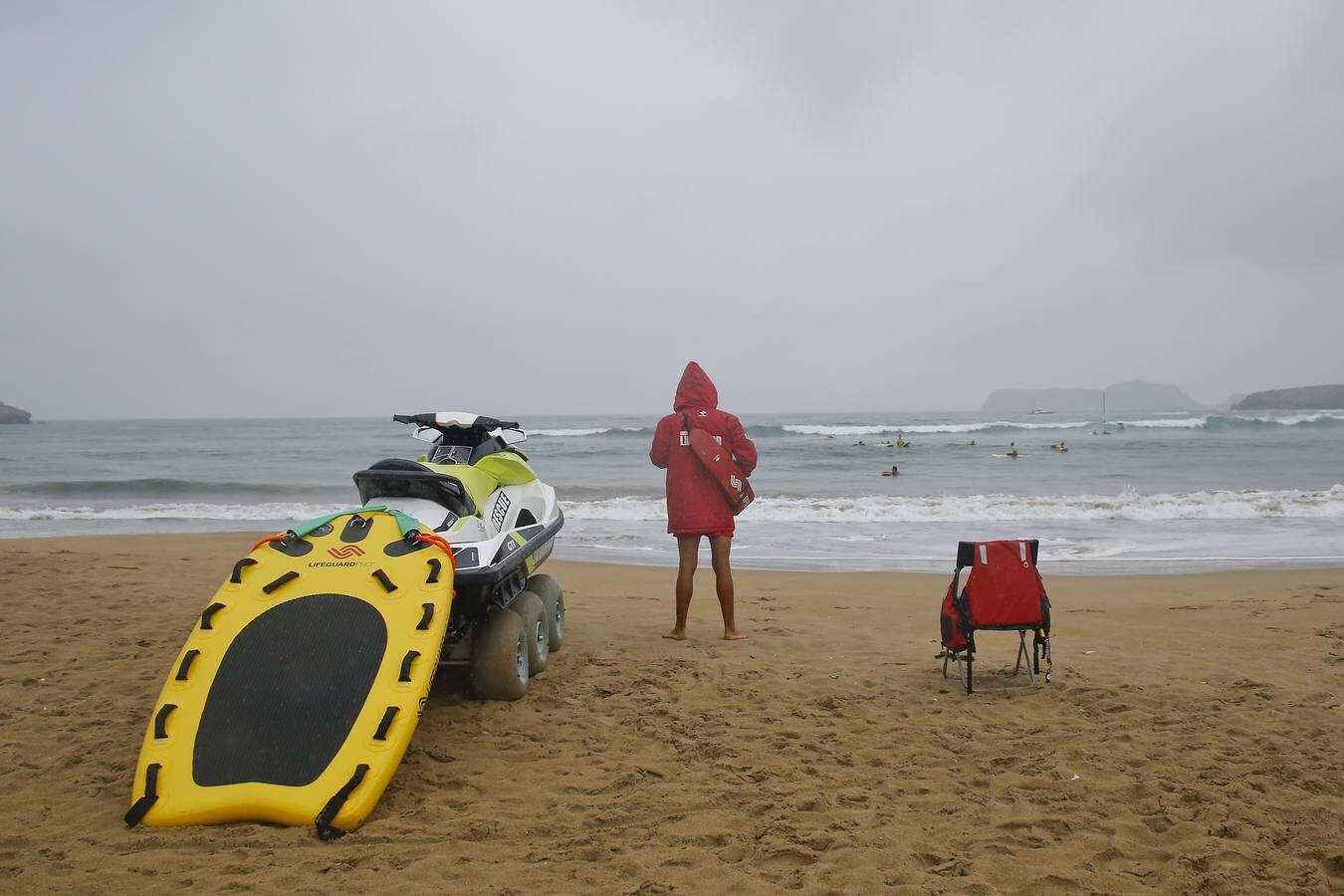 Un socorrista vigila a un grupo de surfistas en la playa de La Concha, en Suances, en un día lluvioso de finales de julio.