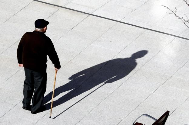 Un anciano camina por la calle ayudado de un bastón.