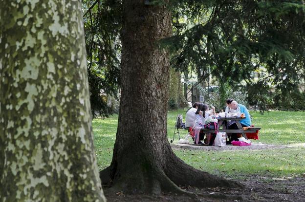 Una familia come en una de las muchas mesas que hay en el parque de Alceda.