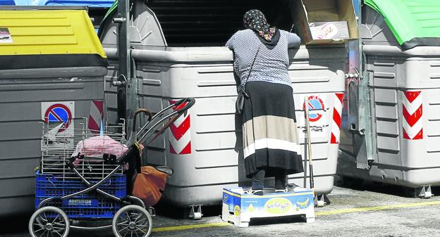 Una mujer busca comida en un contenedor de basura en el centro de Torrelavega. :