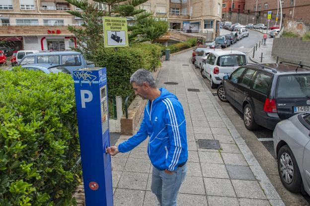 Un hombre saca el tique en el parquímetro para poder dejar su coche aparcado en la zona azul.