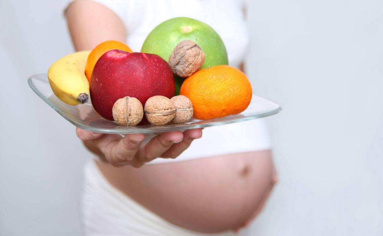 Una mujer embarazada sostiene un plato con fruta y nueces.