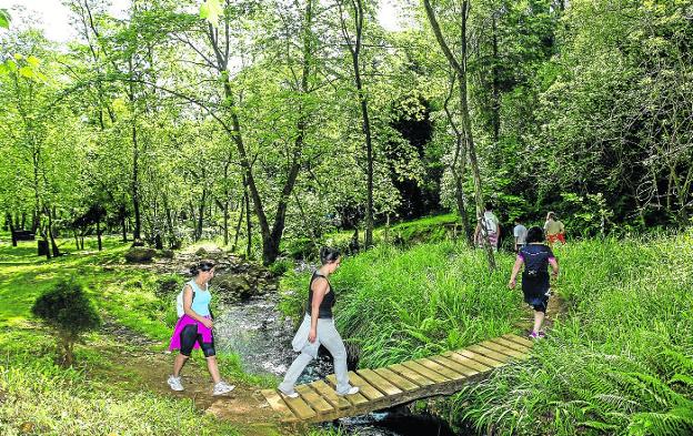 Un grupo de senderistas cruza un arroyo en el parque de La Viesca, cerca del Barrio Covadonga