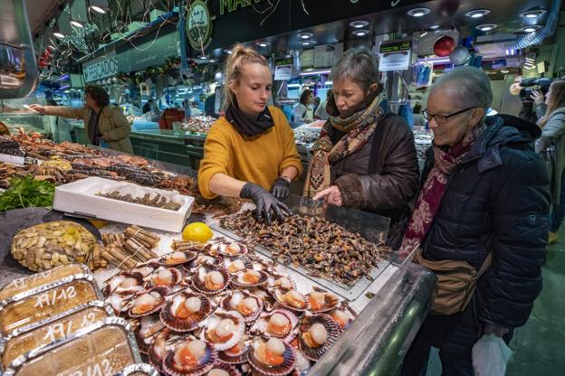 Una trabajadora muestra los percebes a dos clientas en el Mercado de La Esperanza. 