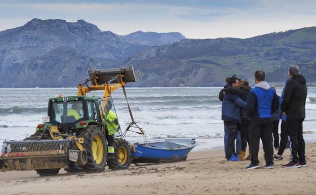 Familiares y amigos del pescador fallecido se abrazan en la playa Salvé a la espera de noticias, mientras un tractor remolca la embarcación siniestrada.