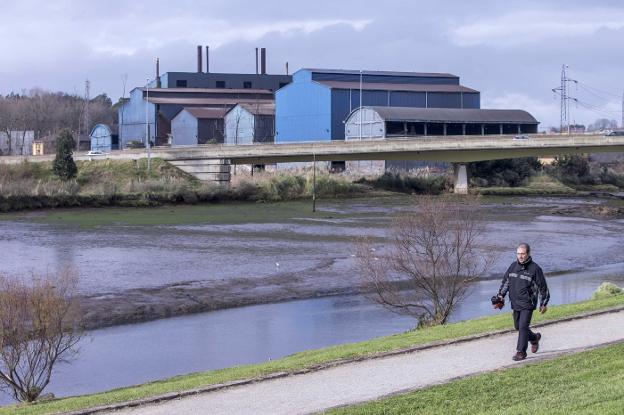 Un hombre pasea junto a la Ría del Carmen, con Ferroatlántica al fondo, entre Camargo y El Astillero.