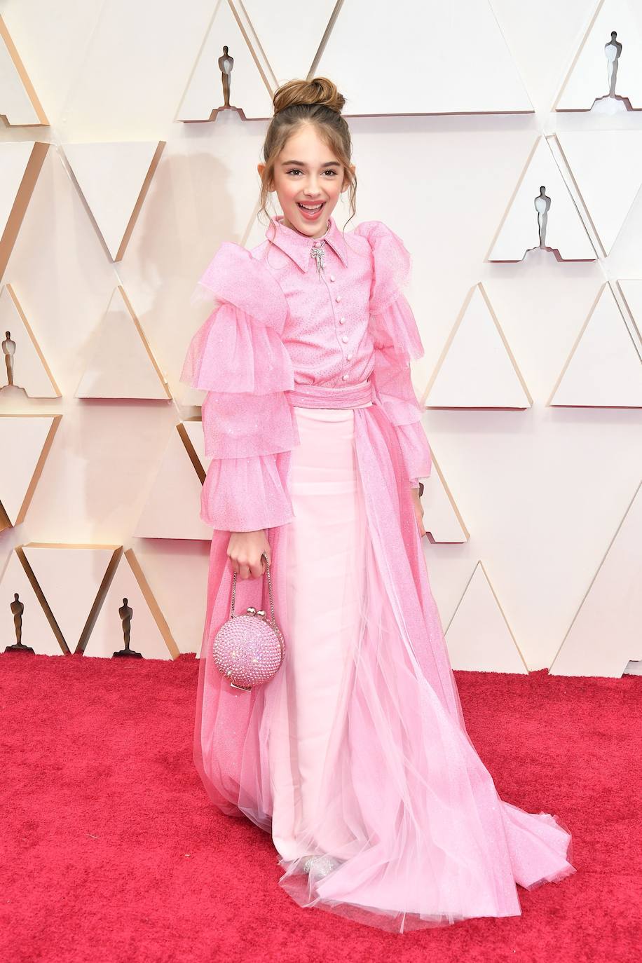 Julia Butters, la jovencísima actriz de Érase una vez en… Hollywood, hace su debut en la alfombra roja de los Oscar con un estilismo un tanto edulcorado, firmado por Christian Siriano, aunque perfecto para una niña de 10 años. A base de tul rosa y mangas con mucho volumen, ha sido supuesto una bocanada de aire fresco a esta nueva edición de la alfombra roja. Como curiosidad, dentro de su ‘cluth’ cuajado de cristales rosas, llevaba un sándwich de pavo. ‘No me gusta la comida que hay aquí’, reconocía.