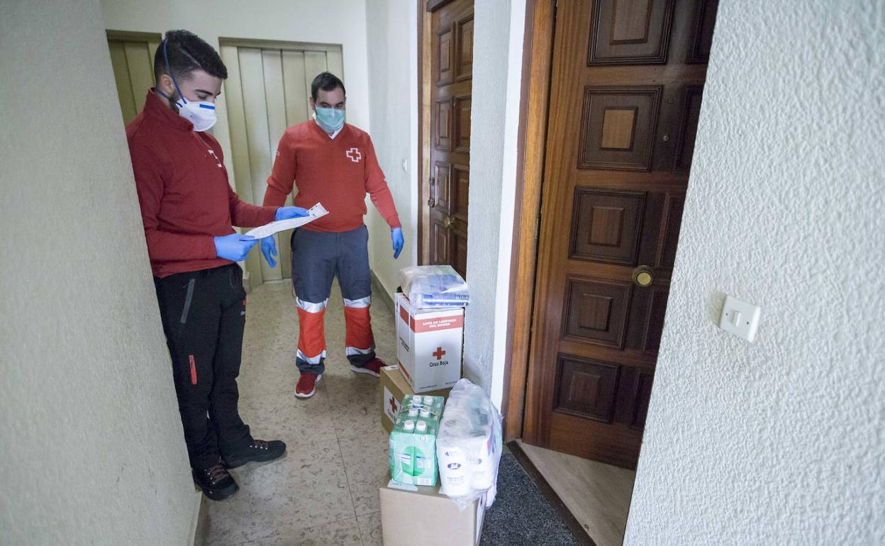 Dos voluntarios de Cruz Roja, muy importantes para que muchas personas dependientes puedan sobrellevar el confinamiento, reparten comida en una vivienda.
