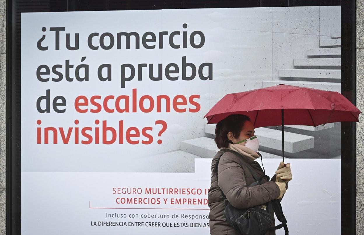 Una mujer con mascarilla pasa delante de un cartel publicitario de una entidad bancaria. EFE /FERNANDO VILLAR