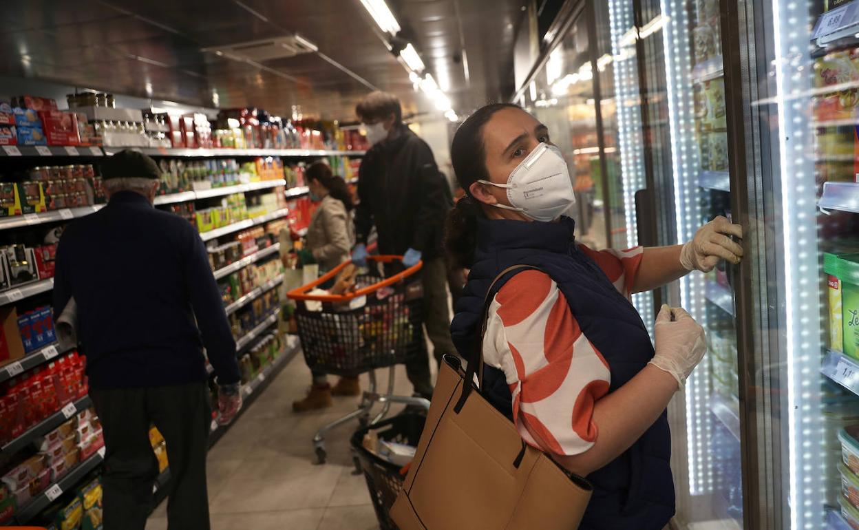 Varias personas compran en un supermercado, algunas con mascarilla.