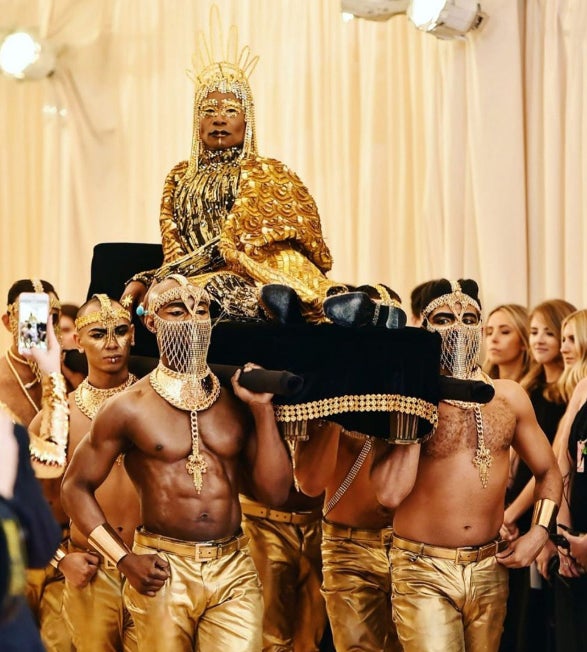 A Billy Porter le llevaron a cuestas. De por sí, los estrafalarios estilismos de Billy Porter tienden a llamar la atención, pero en una gala MET, donde la fantasía campa a sus anchas por la alfombra roja, las posibilidades de dejarnos ojipláticos se triplican. Ni corto ni perezoso (o sí), el actor apareció el año pasado porteado por seis hombres sin camisa al más puro estilo Cleopatra. Toda una oda al exceso gracias a The Blonds, que le cubrió de dorado de arriba abajo y culminó su look con unas alas, una suerte de peluca con cadenas de oro de 24 quilates y unos botines de Giuseppe Zanotti. El maquillaje, también en oro, fue obra de Pat McGrath. Una imagen llena de referentes que, sin duda, nos traslada a la película protagonizada por Elisabeth Taylor en 1963, en la que daba vida a la faraona egipcia más famosa de todos los tiempos.