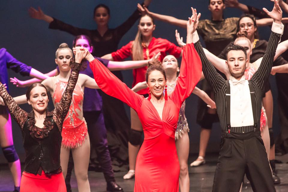 Espectacular con un vestido rojo con escote cruzado, manga ancha y maxi-pendientes, saludando al público al finalizar un espectáculo de danza.