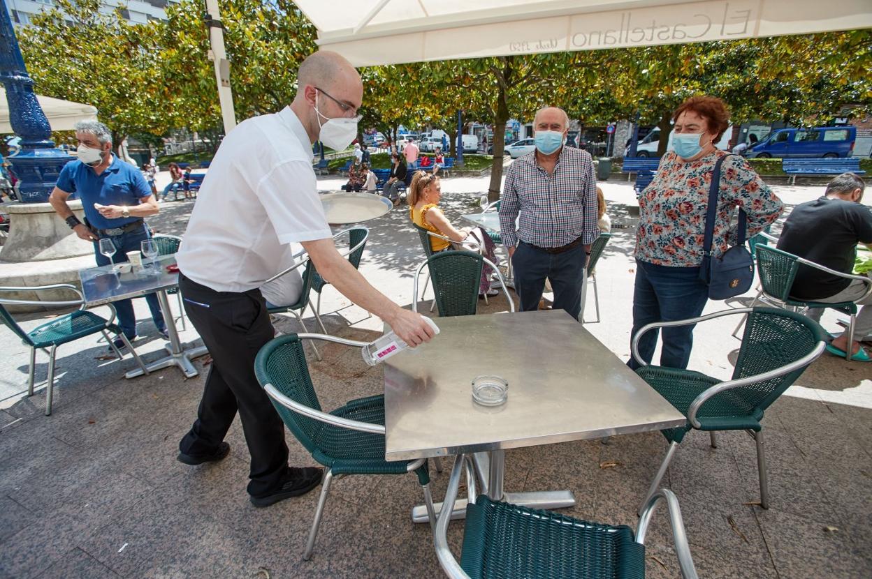 Un camarero desinfecta la mesa de una terraza en Santander antes de que sienten unos clientes. 