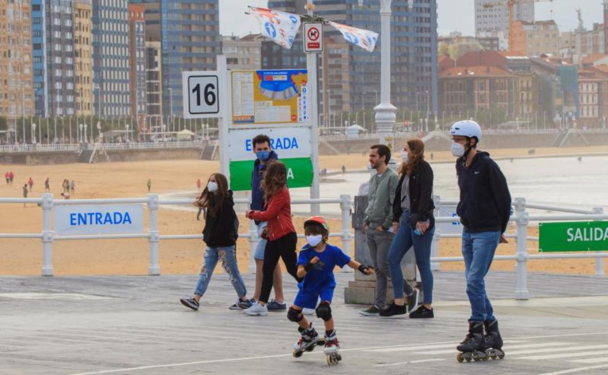 Personas pasean por el paseo marítimo de la playa de San Lorenzo de Gijón 