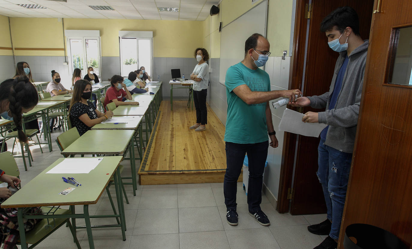 Un profesor echa gel hidroalohólico a un alumno antes de entrar al exámen. 