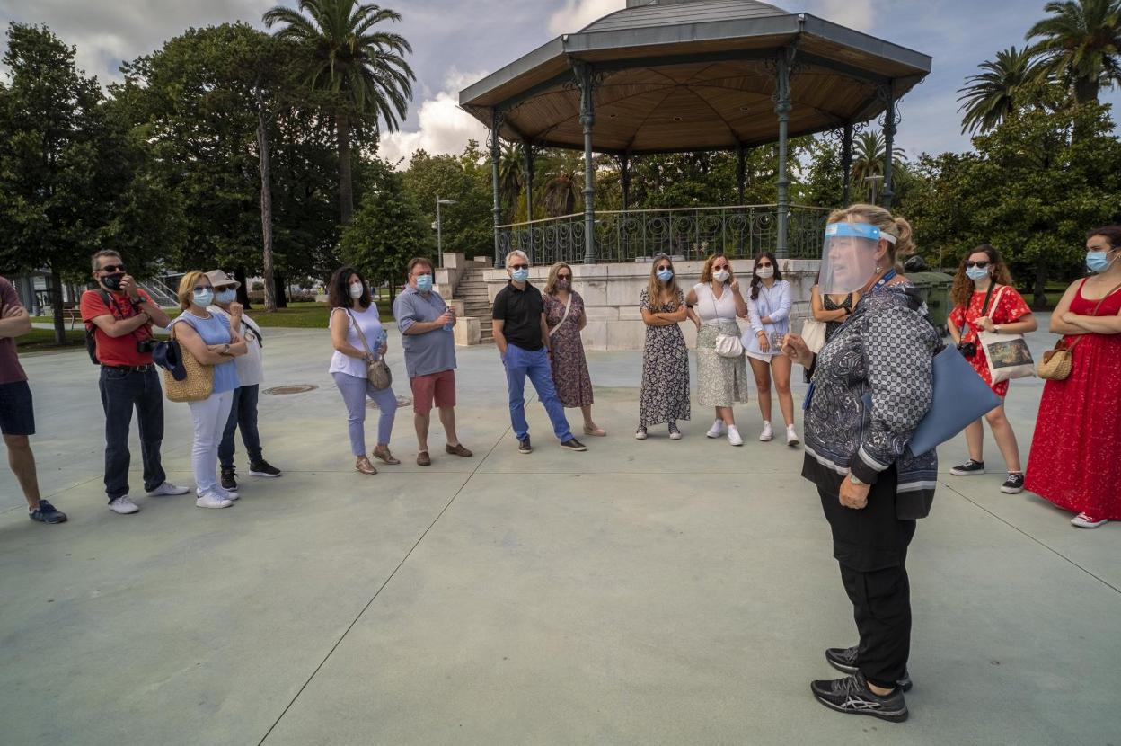 Visitantes españoles, con mascarilla, escuchan las explicaciones en castellano de una guía turística, junto al escenario de los Jardines de Pereda. 