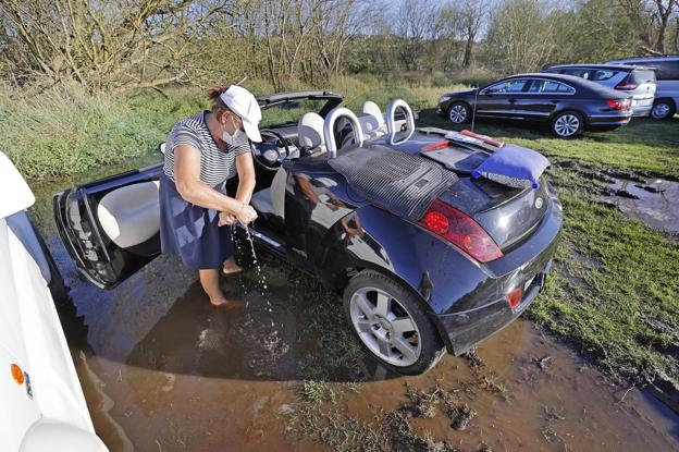 Una mujer achica el agua que le entró en el vehículo aparcado, como otra veintena más, en una parcela cerca del campo de golf.