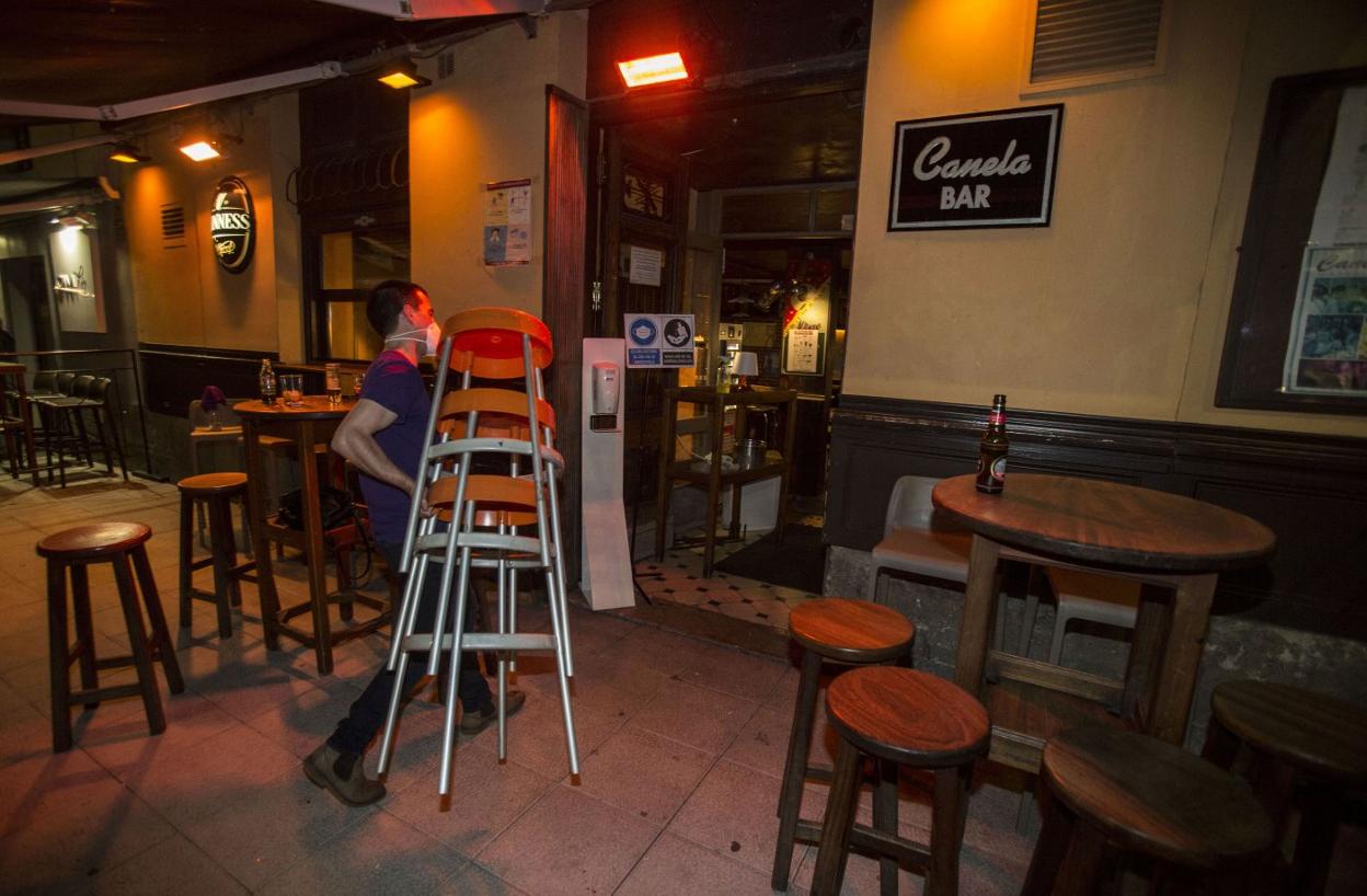 Un trabajador del bar Canela, en Cañadío, recoge las mesas del local para cumplir con el horario de cierre de la hostelería