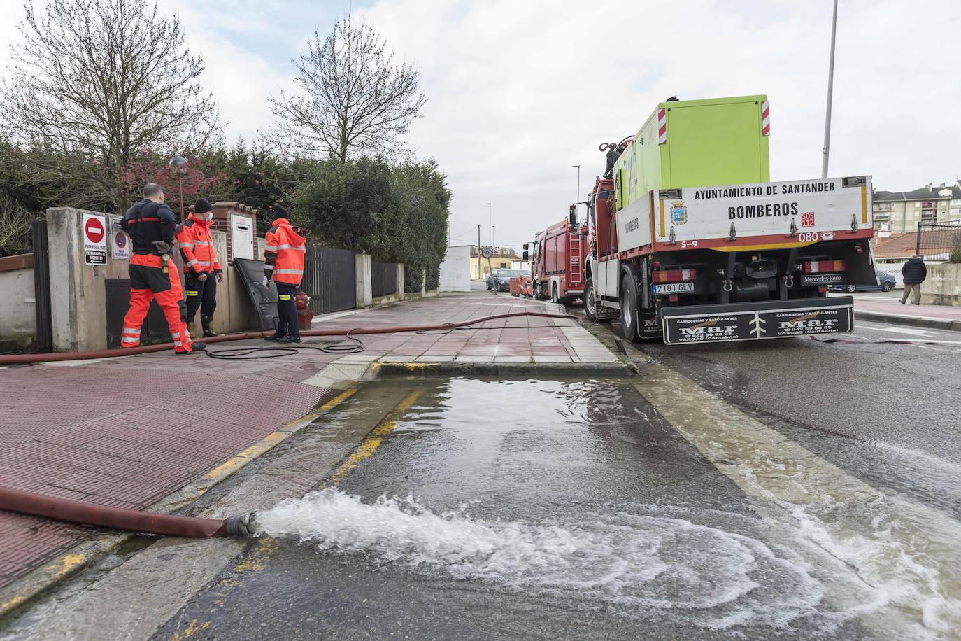 Operarios clavan tablones y extienden una capa de tierra a modo de dique para evitar que el agua vuelva a inundar el barrio de Santiago el Mayor (Nueva Montaña), mientras el vecindario sigue limpiando el barro, colocando sacos a las puertas de sus casas y los bomberos achican el agua acumulada en bajos y garajes.