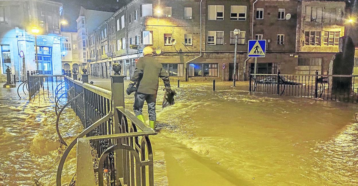 Imagen de la noche del 19 de diciembre de 2019 en la que un hombre, en la calle Deltebre, en Reinosa, trata de cruzar el puente sobre el Ebro, totalmente rebasado por el agua