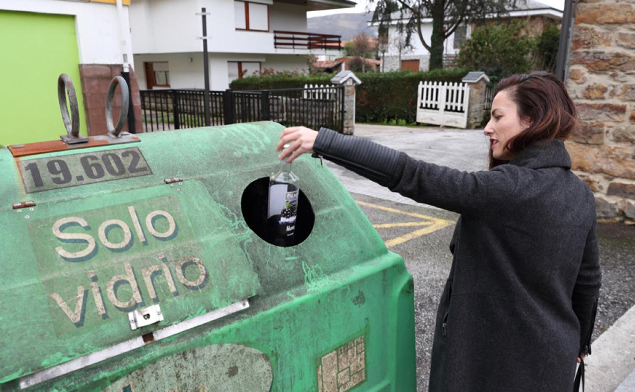 Una joven tira una botella en el contenedor verde de vidrio en Cabezón de la Sal. 