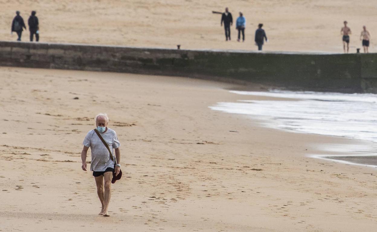 Un hombre con la mascarilla puesta pasea por la playa, una imagen que pasará a ser lo habitual, según la nueva normativa estatal. 