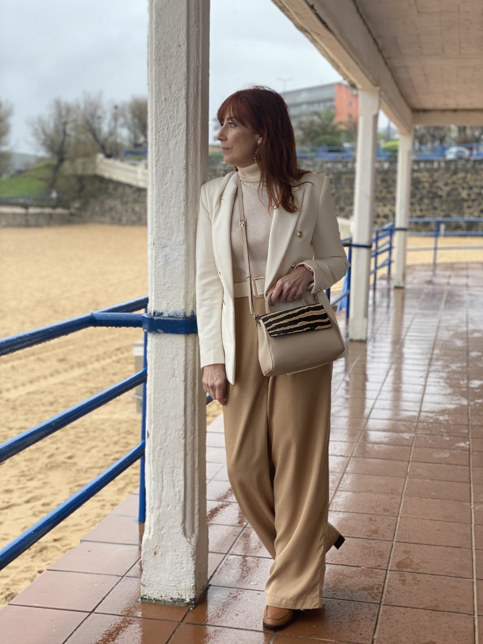 Mi look está formado por un pantalón de talle alto y pata ancha, confeccionado en un tejido con mucha caída y en color camel. Lo he combinado con un jersey en tono crudo casi blanco y una 'blazer' de piqué, también en crudo, con botones dorados. Como complementos, unos mocasines con tacón en color marrón caramelo y un precioso bolso en piel con la solapa realizada en pelo con estampado animal en tonos beige y marrones.