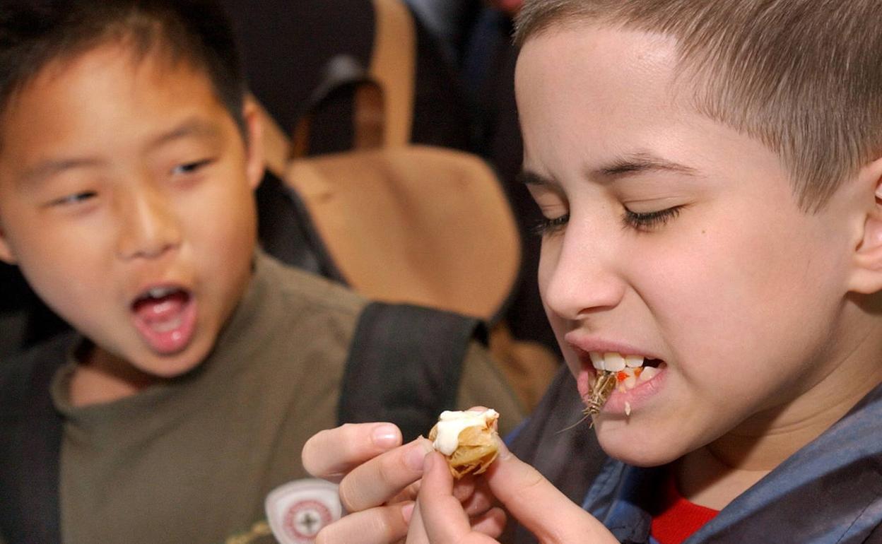 Niños probando una pizza con gusanos, insectos y escorpiones. 