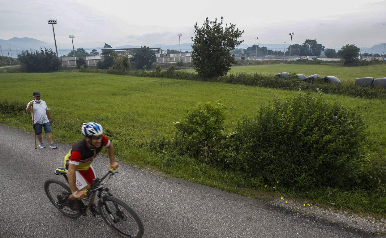 Un ciclista y un viandante pasan junto a los terrenos próximos al campo de fútbol de Santa Ana, en Tanos.