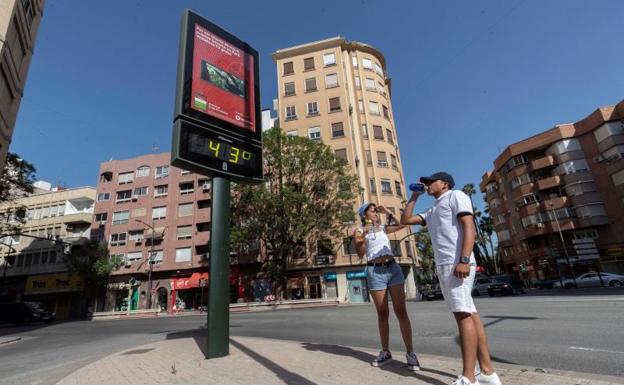 Dos jóvenes beben agua junto a un termómetro que marca 43 grados centígrados, en Murcia 