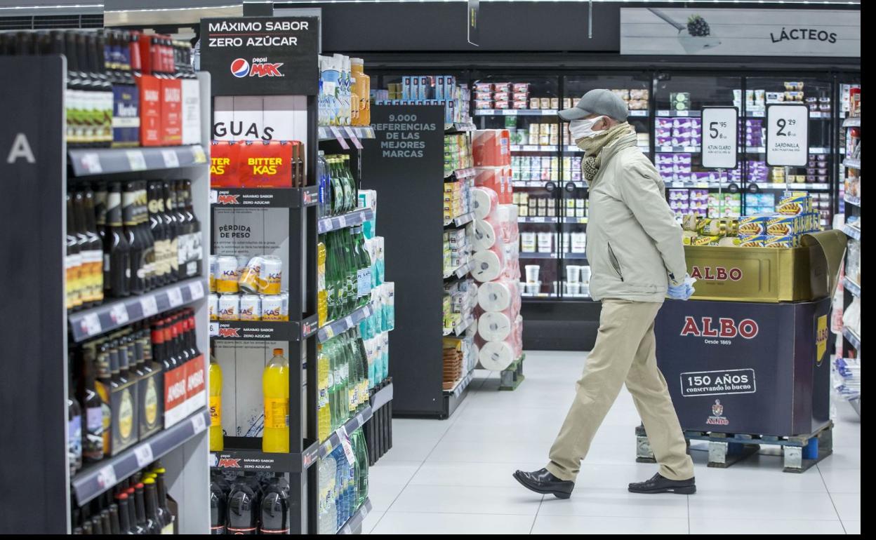 Un cliente se dirige a la zona de bebidas en un supermercado. A su izquierda se encuentra un estante con cervezas de varias marcas. 