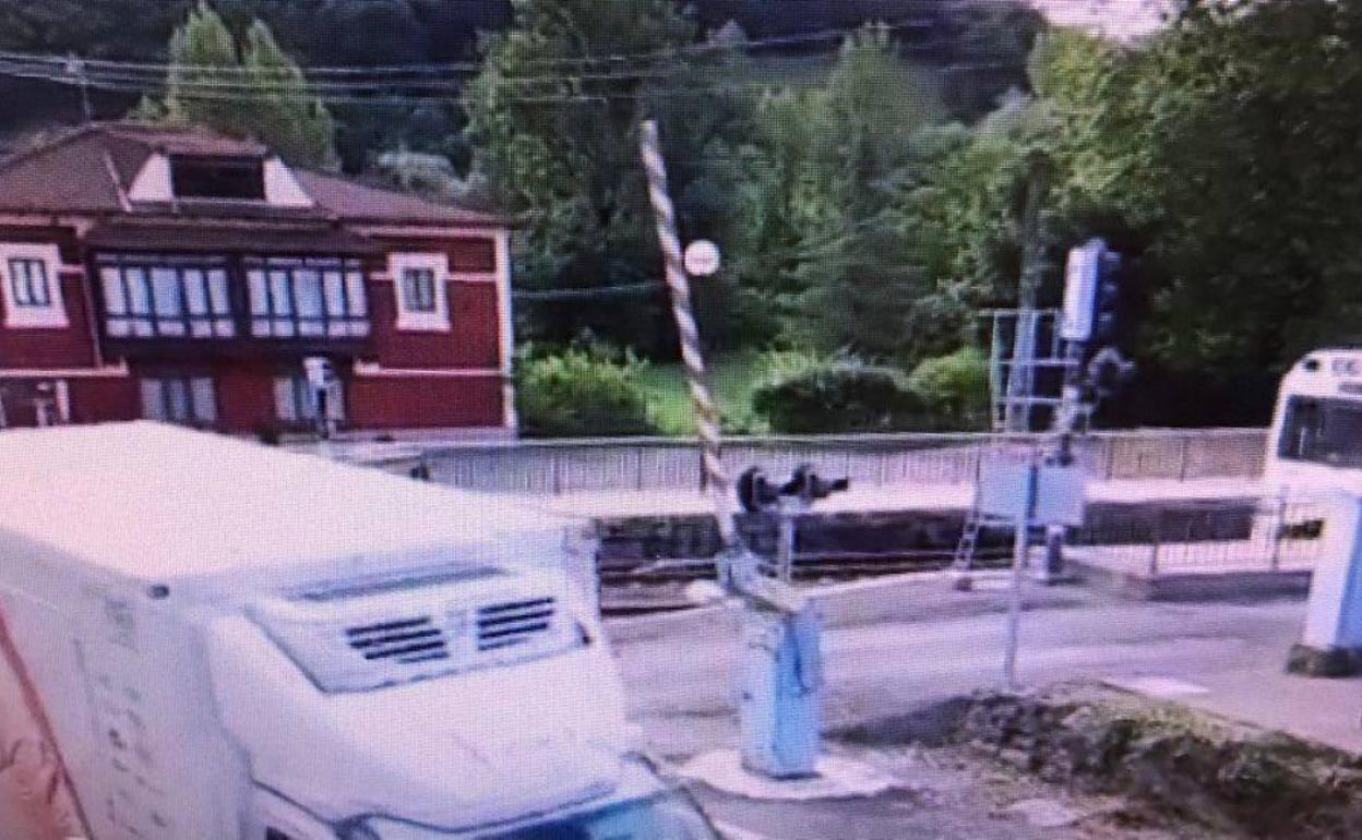 Un pequeño camión cruza el paso a nivel, que tiene las barreras levantadas, poco antes de la llegada de un tren.