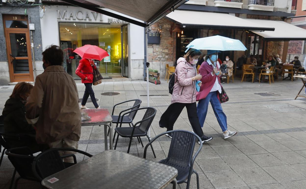 Varias personas caminan con paraguas o se refugian de la lluvia bajo los toldos en Santander. 