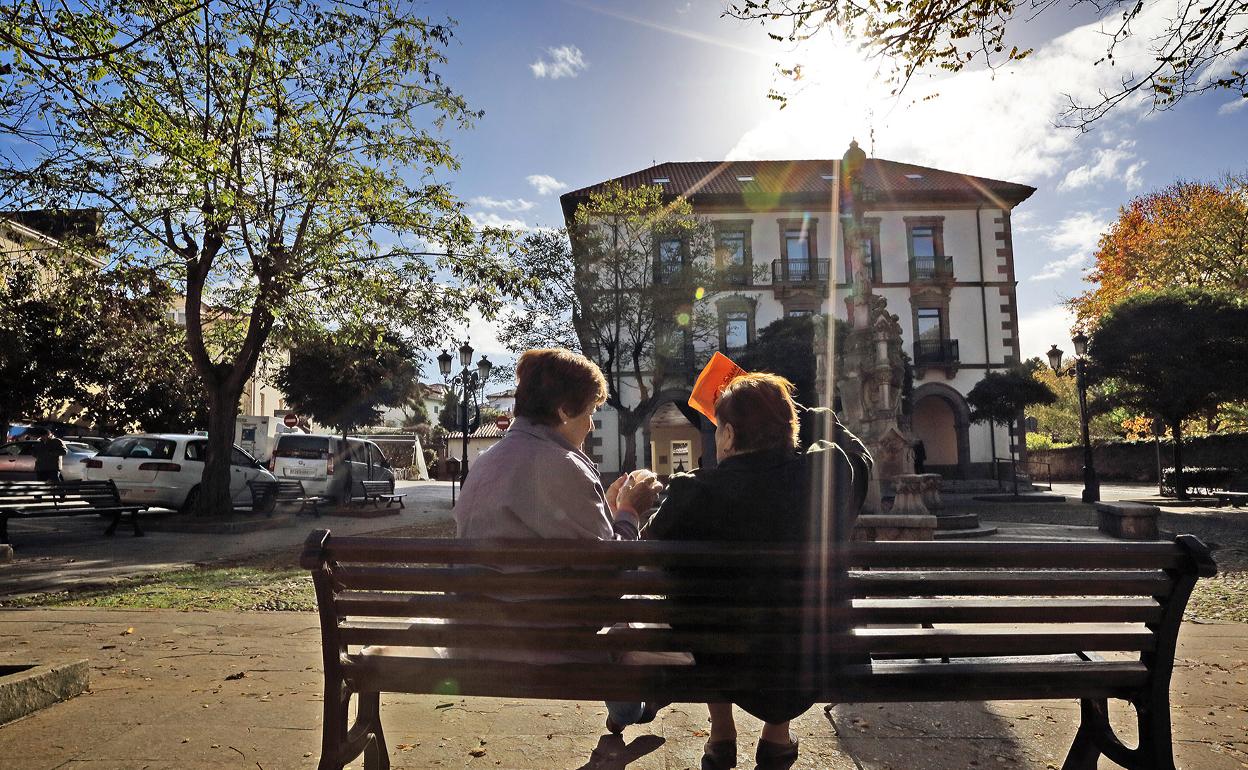 Dos mujeres charlan en la plaza de la fuente Tres Caños en Comillas. 