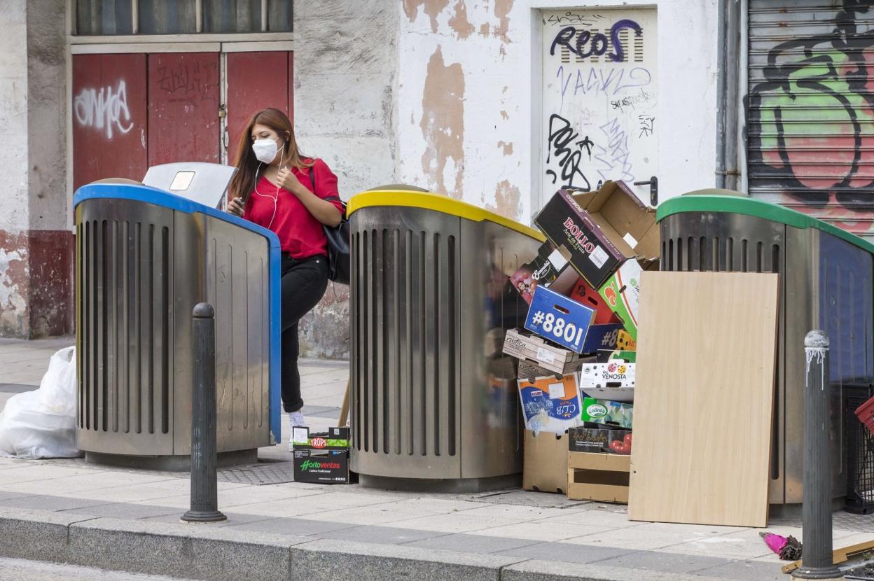 Una mujer abre un contenedor mientras junto a los que tiene al lado se amontonan las cajas y otros restos.