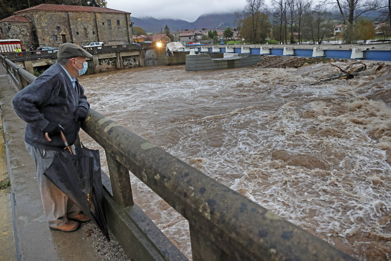 Un señor observa el caudal del río Saja a a su paso por el puente de Virgen de la Peña.