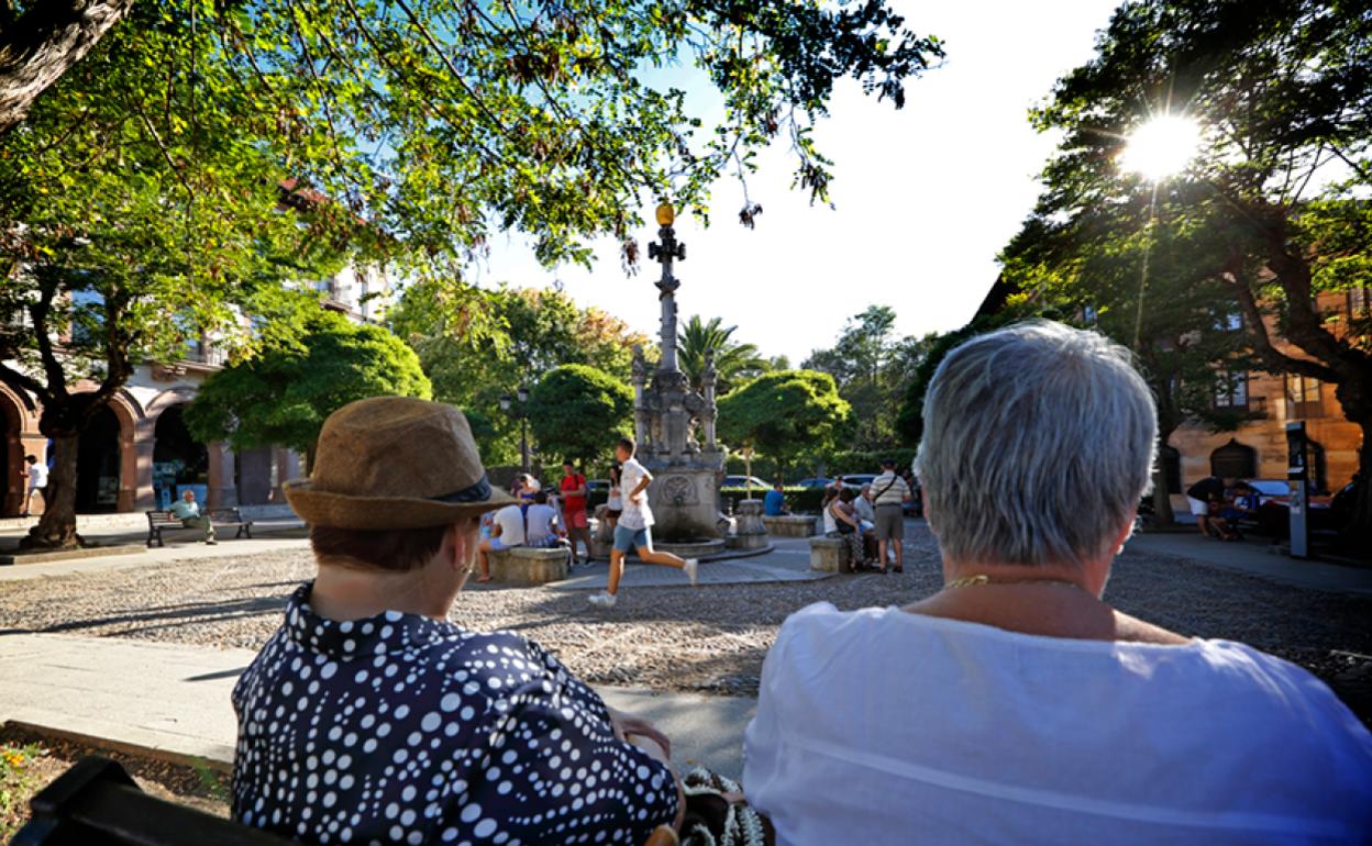 Dos vecinos observan cómo varios niños juegan en la plaza de la Fuente Tres Cantos de Comillas. 