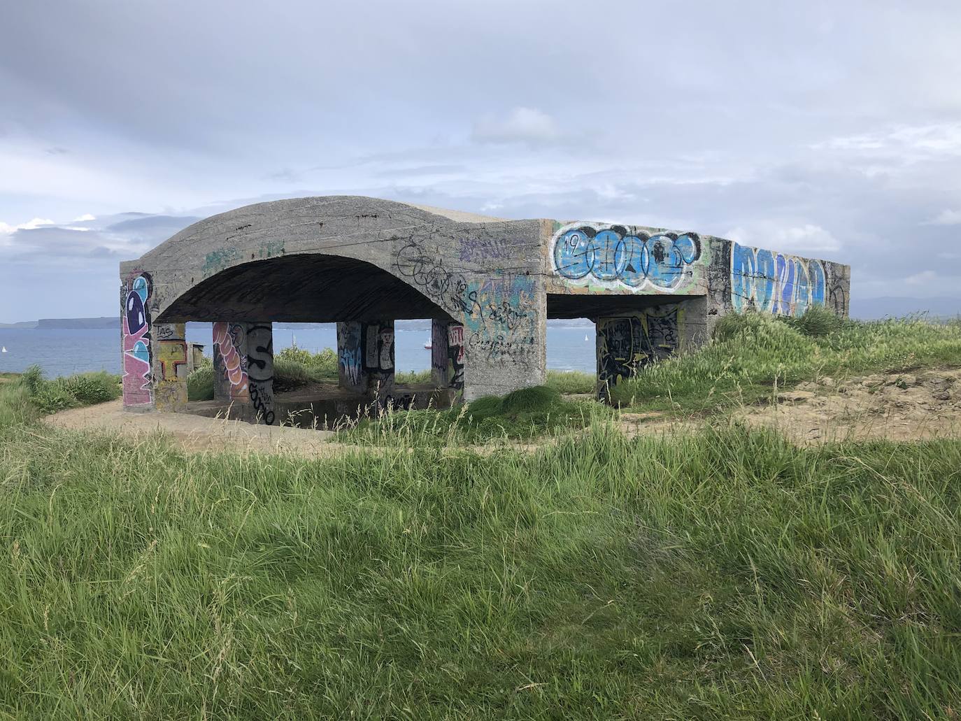 Casamata de artillería de costa. La estructura se conserva en pie, pero muestra deterioro y el hormigón ha desaparecido por zonas, dejando las varillas a la vista.